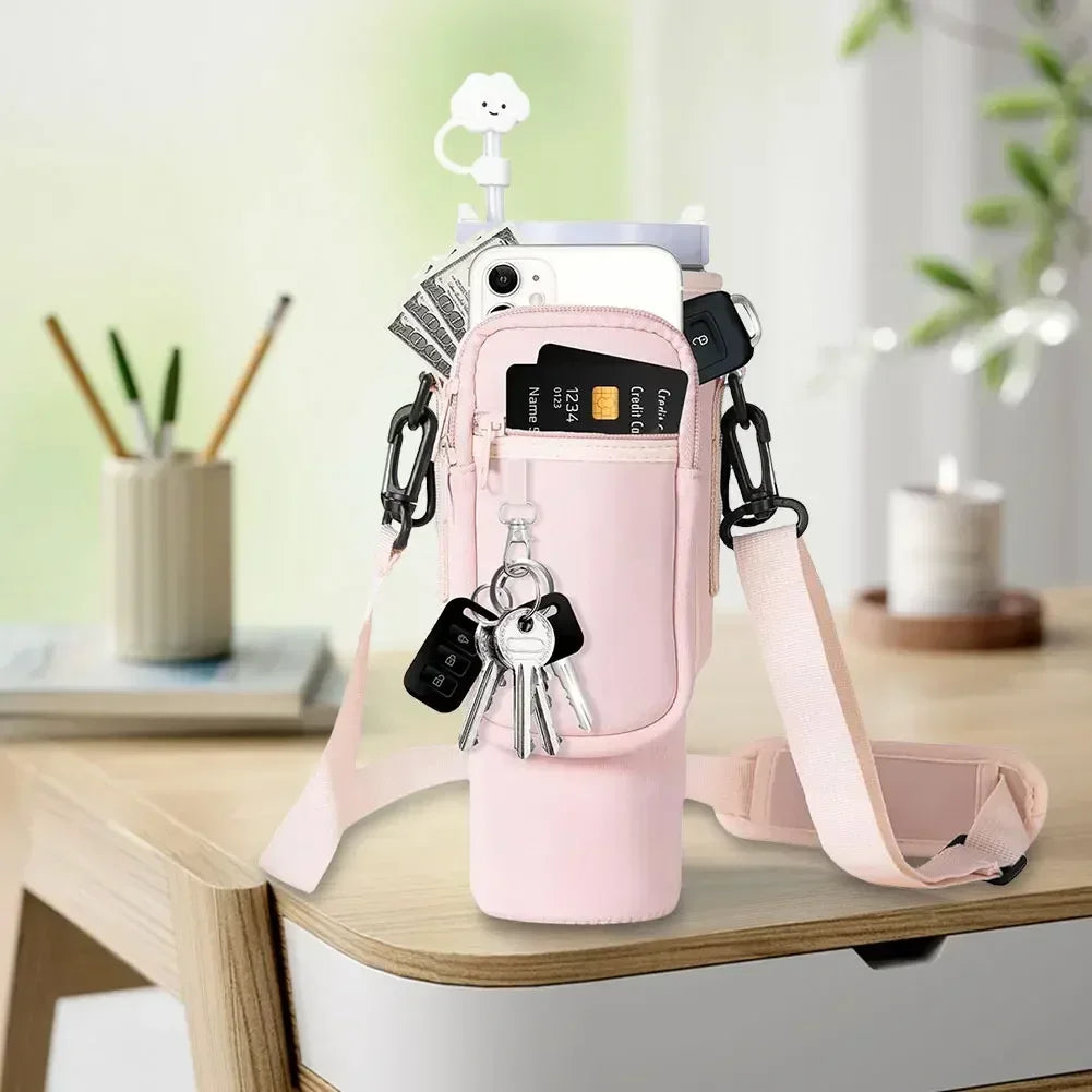 A pink neoprene water bottle carrier bag with a shoulder strap and various keys is displayed on a wooden table.
