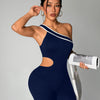 A model wearing a navy blue seamless yoga jumpsuit with a white stripe detail, holding a white bag.