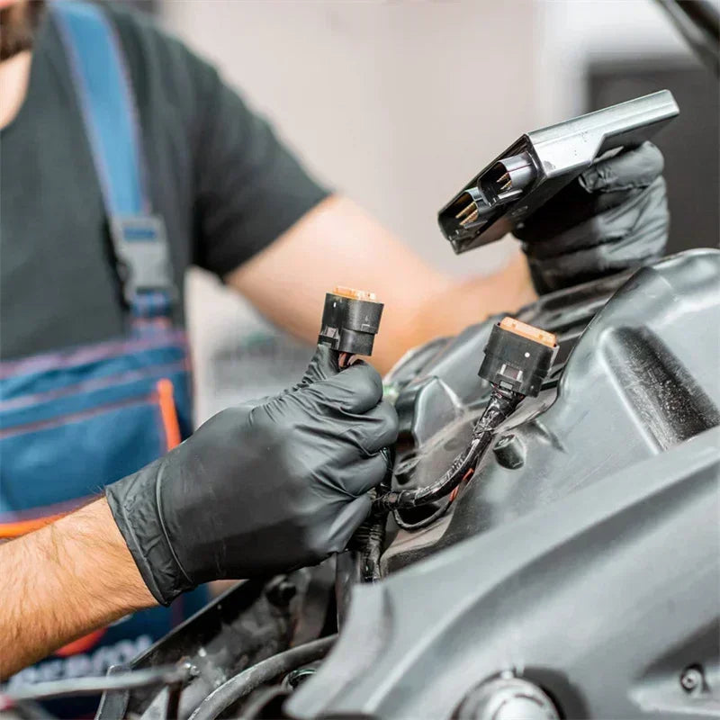 Une personne portant des gants en nitrile noirs travaille sur un composant moteur de voiture avec un outil spécialisé.