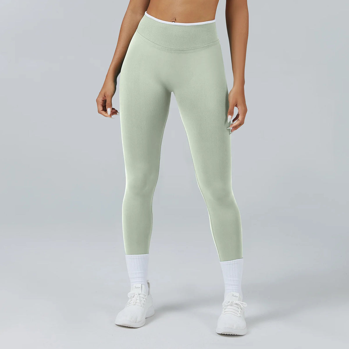 A woman wearing light sage green high-waist yoga leggings and white socks.