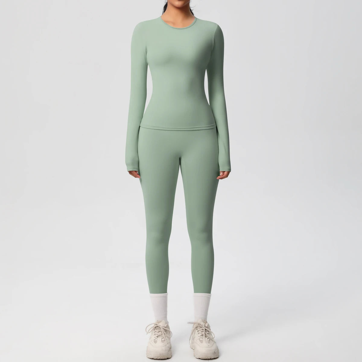 A woman wearing a long-sleeved, fitted, sage green performance yoga and gym set with white socks and shoes.