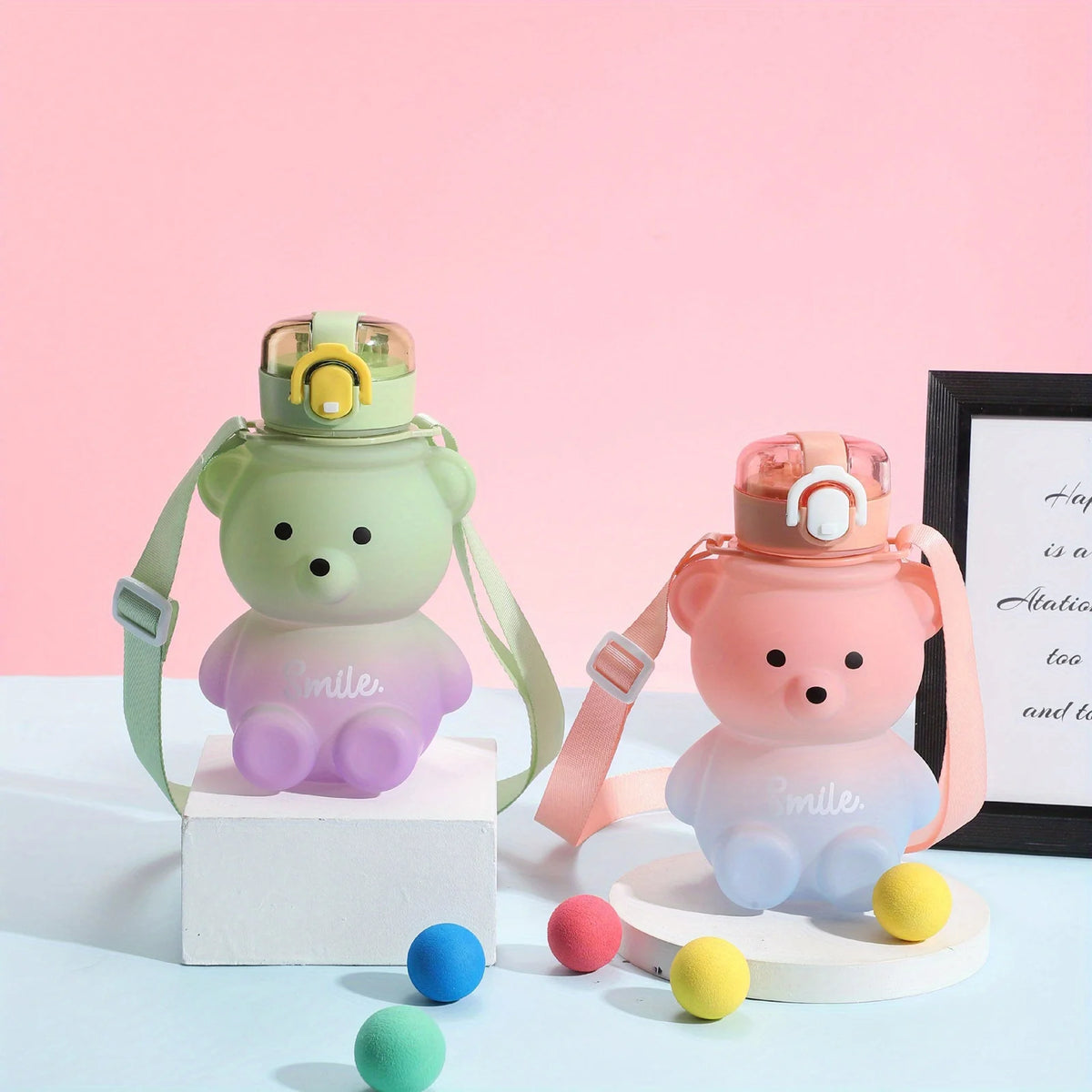 A pink bear-shaped portable water bottle with a straw and strap is displayed on a white surface.