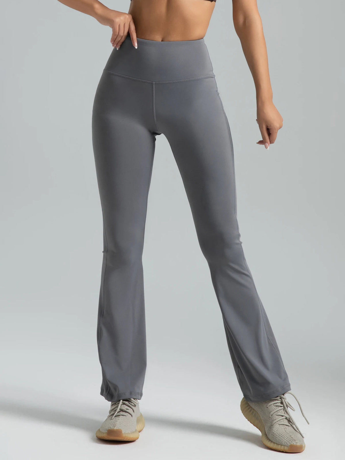 A model is wearing high-waisted grey bootcut yoga pants while standing.