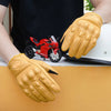 A pair of yellow leather motorcycle riding gloves resting on a light-colored surface next to a red motorcycle.