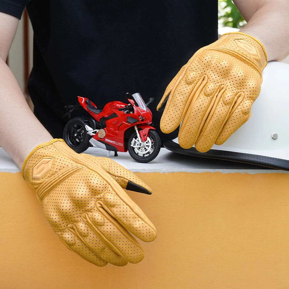 A pair of yellow leather motorcycle riding gloves resting on a light-colored surface next to a red motorcycle.