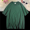 Dunkelgrifes, oversized Baumwoll-T-Shirt einer Frau auf weißem Plüsch neben Sonnenbrille und Teddybär.