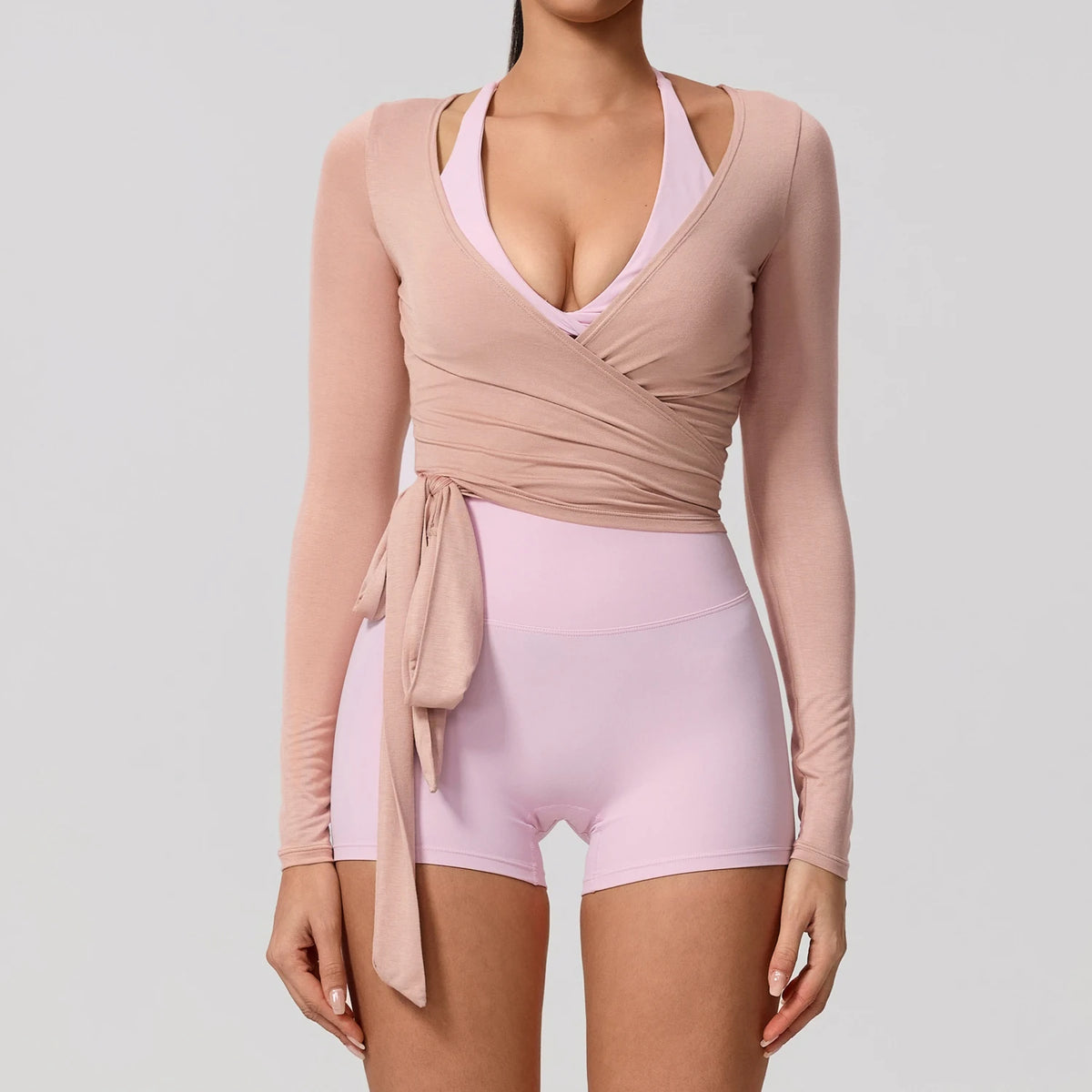 A woman wearing a light pink long sleeve top and matching shorts, featuring a wrap detail.