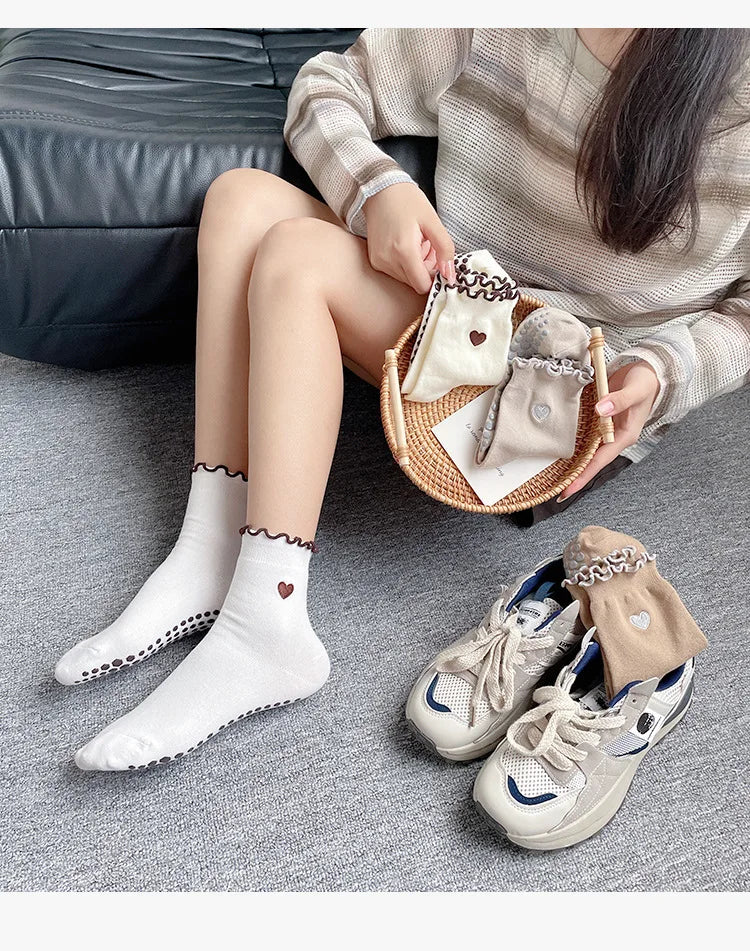 A person is holding a set of beige embroidered yoga socks and a pair of light gray canvas sneakers on a gray background.