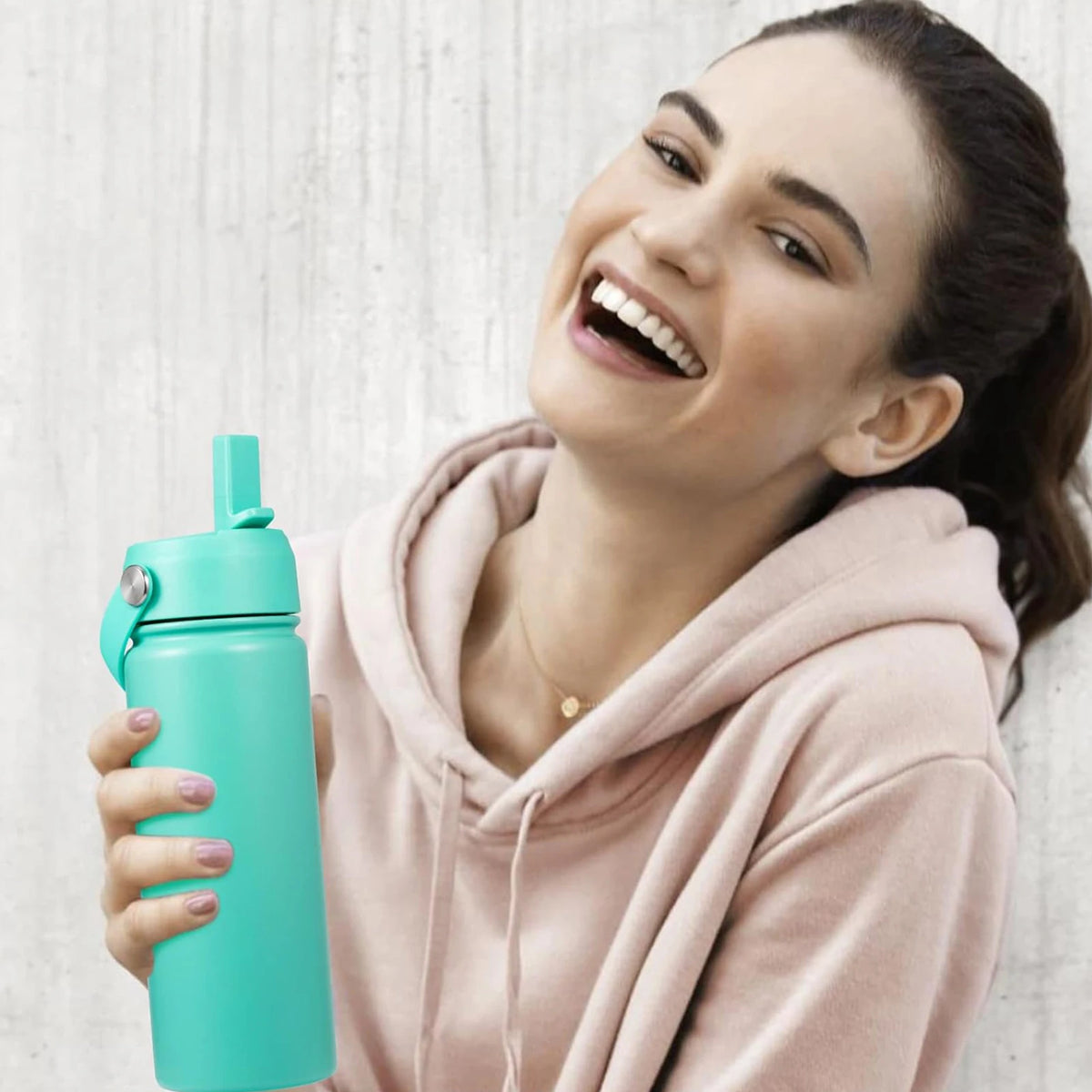 Eine Frau hält eine türkisblaue Flasche mit versieglertem Deckel und trägt einen rosa Hoodie.