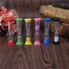 A set of six colorful sand timer hourglasses in various colors, displayed on a wooden surface next to a book.