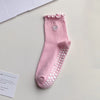 A pink yoga sock with a ruffled cuff and a heart embroidery on the toe, displayed on a white surface.