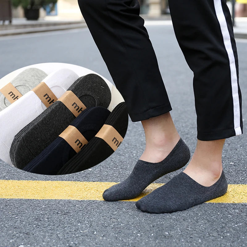 A pair of multi-colored breathable cotton ankle socks are laid out on asphalt next to a person's legs.