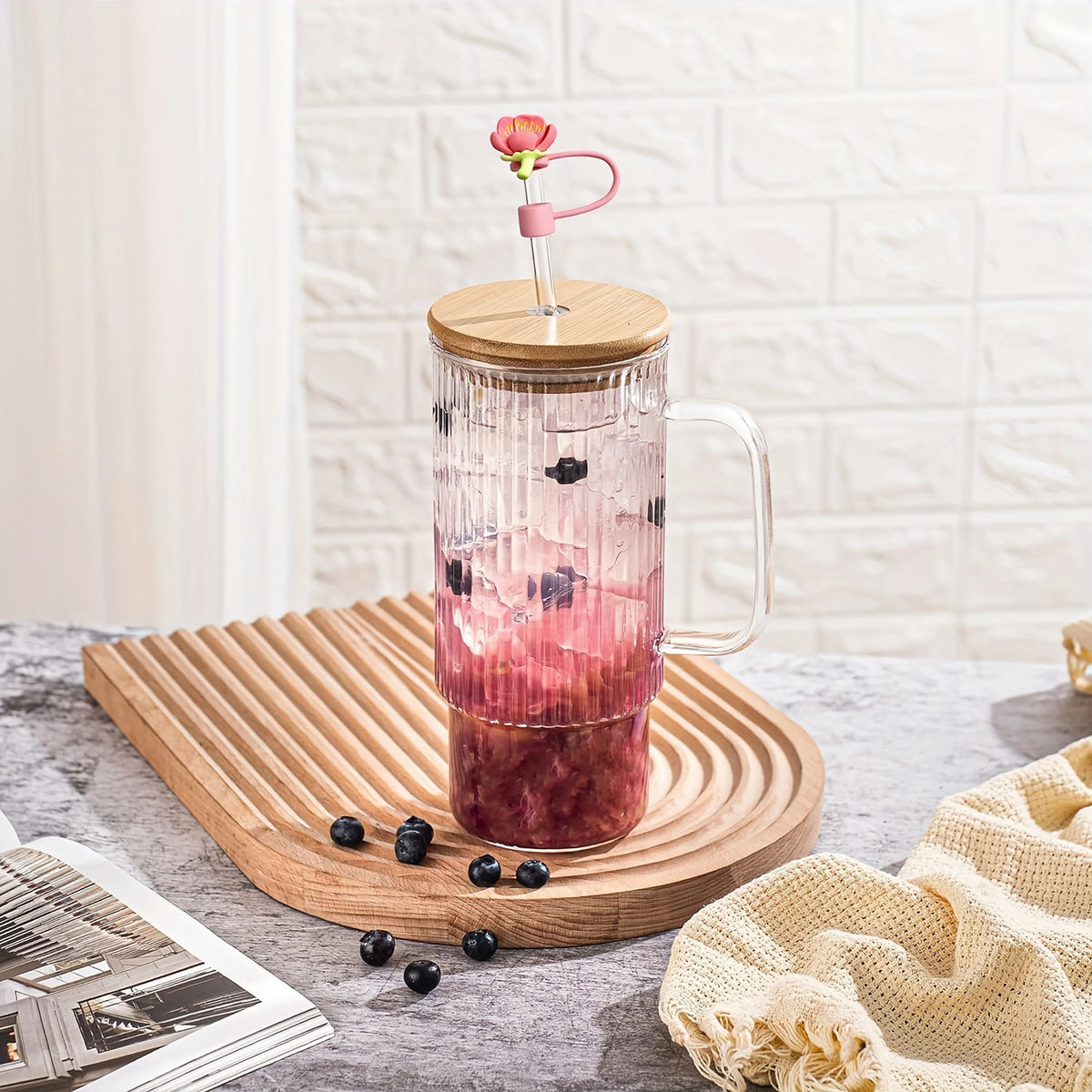 A glass tumbler filled with a pink beverage and topped with a silicone straw cover and a pink straw.