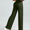 A woman models high waisted olive green yoga pants with a white top and white sneakers.