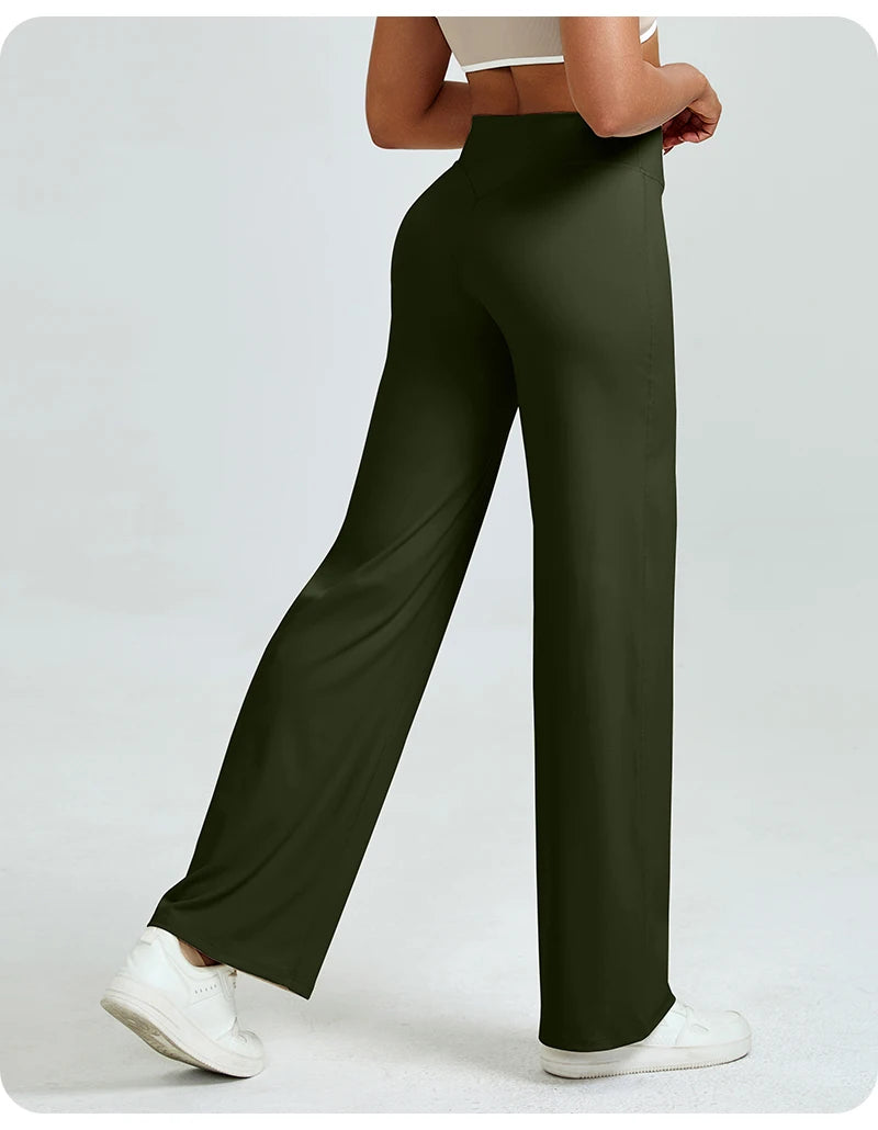 A woman models high waisted olive green yoga pants with a white top and white sneakers.