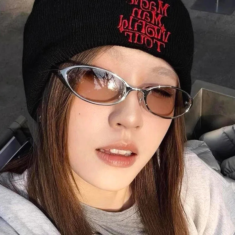 A close-up photo of a woman wearing retro oval sunglasses with a metal frame and a black knit beanie.