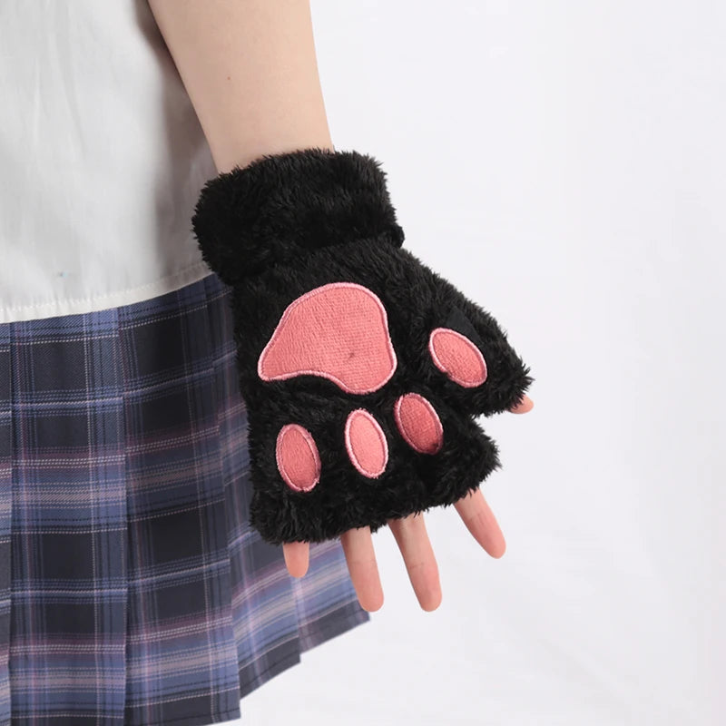 Black plush cat claw mittens with pink paw pads worn on a hand against a plaid skirt.