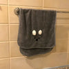 A gray soft coral fleece face towel hanging on a metal rack against a tiled wall.