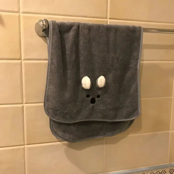 A gray soft coral fleece face towel hanging on a metal rack against a tiled wall.