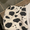 A white and black cow print face towel draped over a white toilet tank.