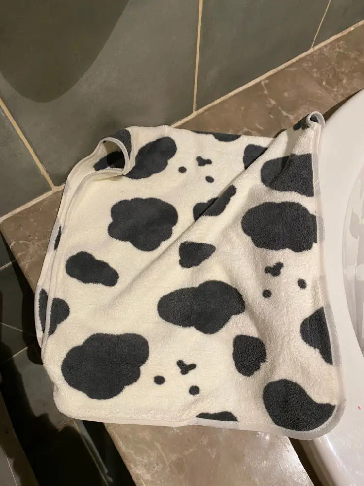A white and black cow print face towel draped over a white toilet tank.