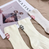 A pair of cream-colored knitted socks with red embroidery displayed next to a magazine.