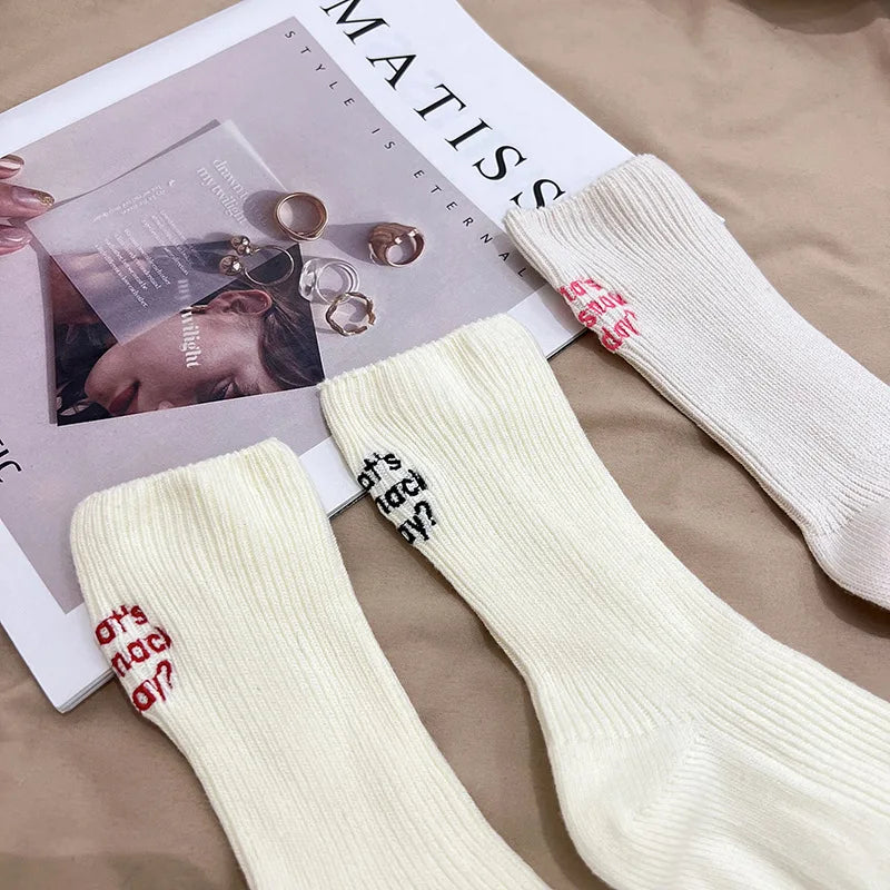 A pair of cream-colored knitted socks with red embroidery displayed next to a magazine.