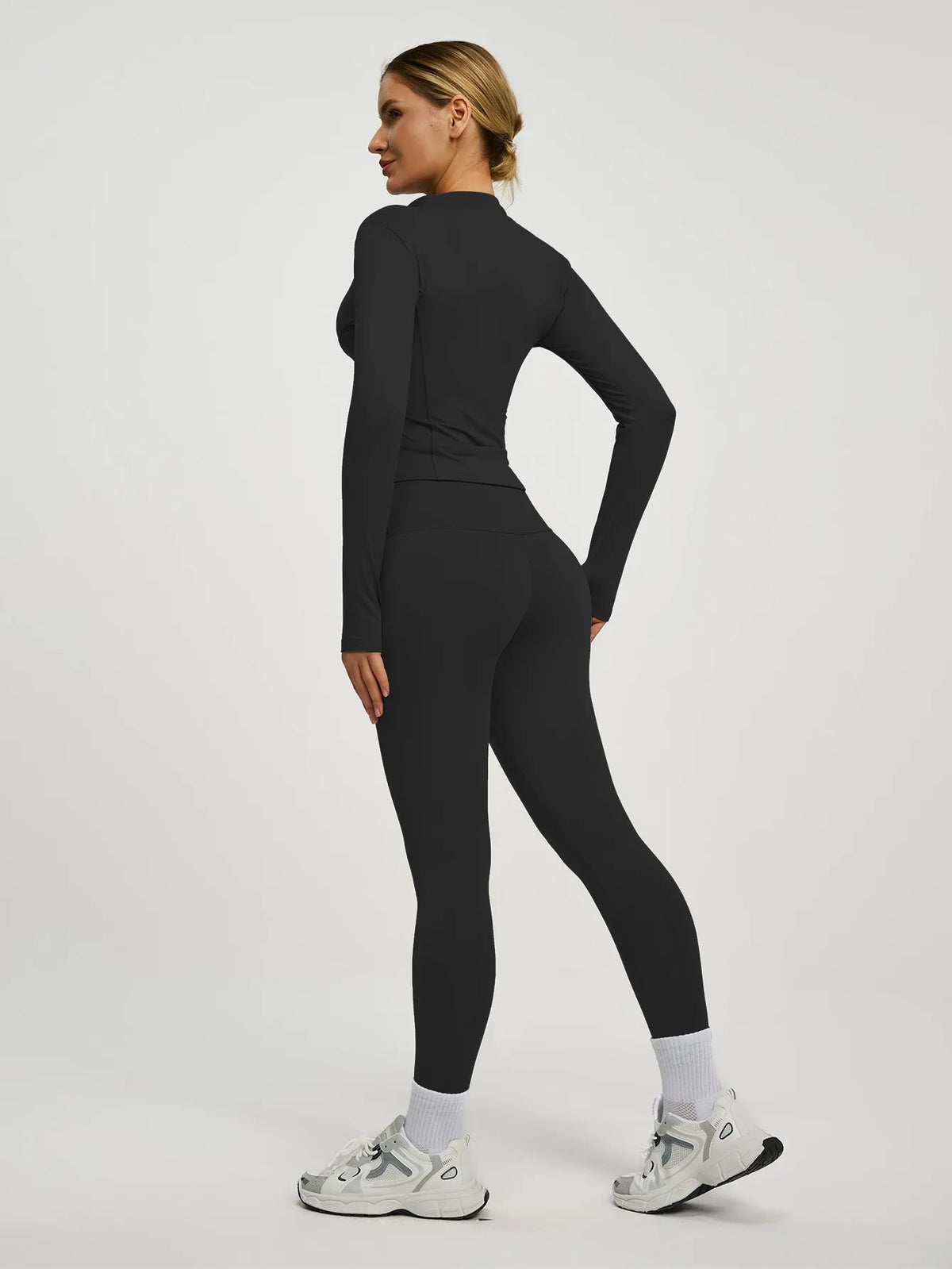 Eine Frau trägt ein schwarzes Langarm-Top und Leggings eines zwei-teiligen Yoga-Sportsets.