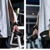 A person wearing a white shirt and dark pants is demonstrating black gym wrist wraps for strength training.