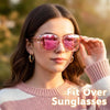 A woman models pink-tinted wrap-around sunglasses with glasses compatibility against a blurred outdoor background.