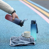 A hand pours water from a purple sports bottle into a white mug on a blue textured surface.