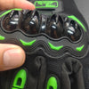 A close-up of black motorcycle riding gloves showing the fingers and palm area with green accents.