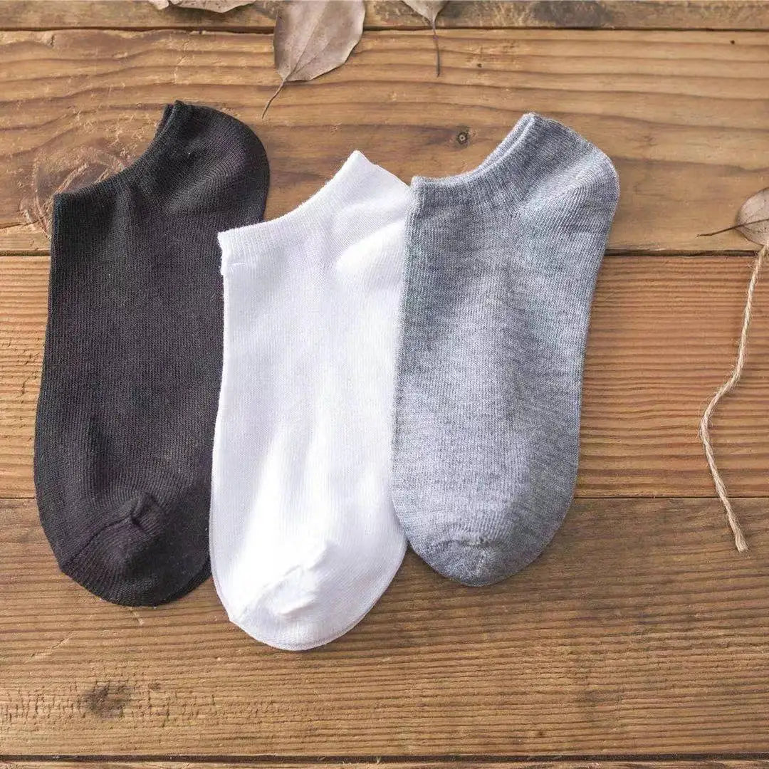 Tres pares de calcetines de algodón transpirables para el tobillo en negro, blanco y gris sobre una superficie de madera.