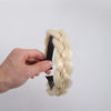 A hand is holding a light blonde twisted braided wig headband.