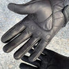 A close-up of black leather motorcycle riding gloves showing the palm and fingers.