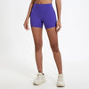 Un mannequin portant un short de yoga et de sport violet à taille haute et des baskets blanches.