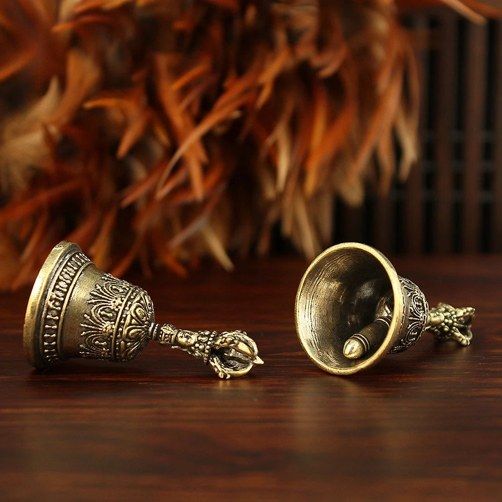 Cloche à tintement en bronze avec poignée ornée et ornement en forme d'oiseau, posée sur une surface en bois sombre.