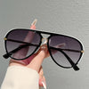 A hand holds a pair of black and white vintage pilot sunglasses with gradient lenses against a gray background.