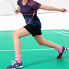 A person wearing a blue shirt and black shorts is playing tennis, with a net visible in the foreground.