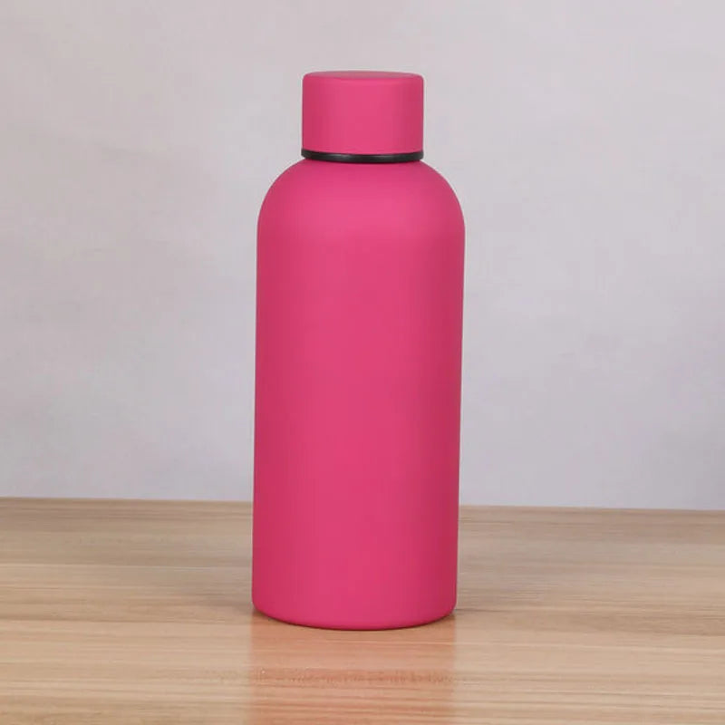 A pink double-layer vacuum thermos cup standing upright on a wooden surface.