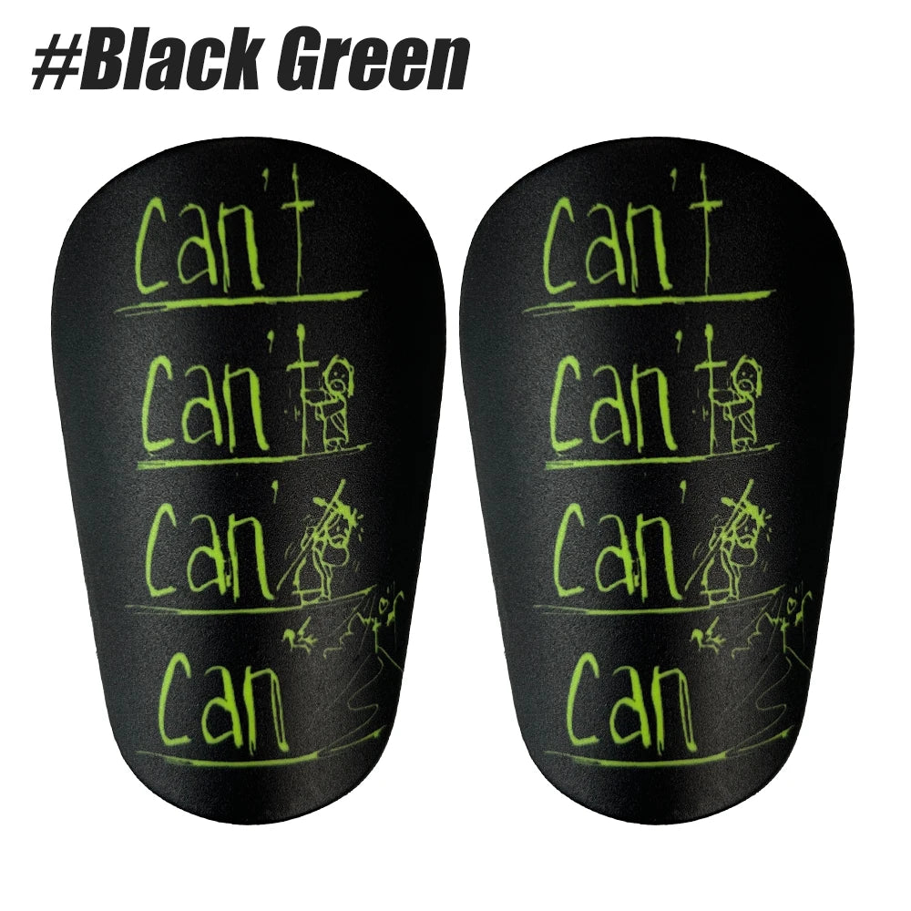 A pair of black shin guards with green text showing 'can' and a stick figure.