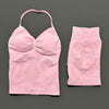 A pink women's seamless backless fitness set top and matching shorts laid flat on a dark gray background.