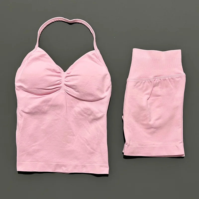 A pink women's seamless backless fitness set top and matching shorts laid flat on a dark gray background.