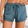 A model wearing teal athletic shorts with mesh pockets and a drawstring waist.