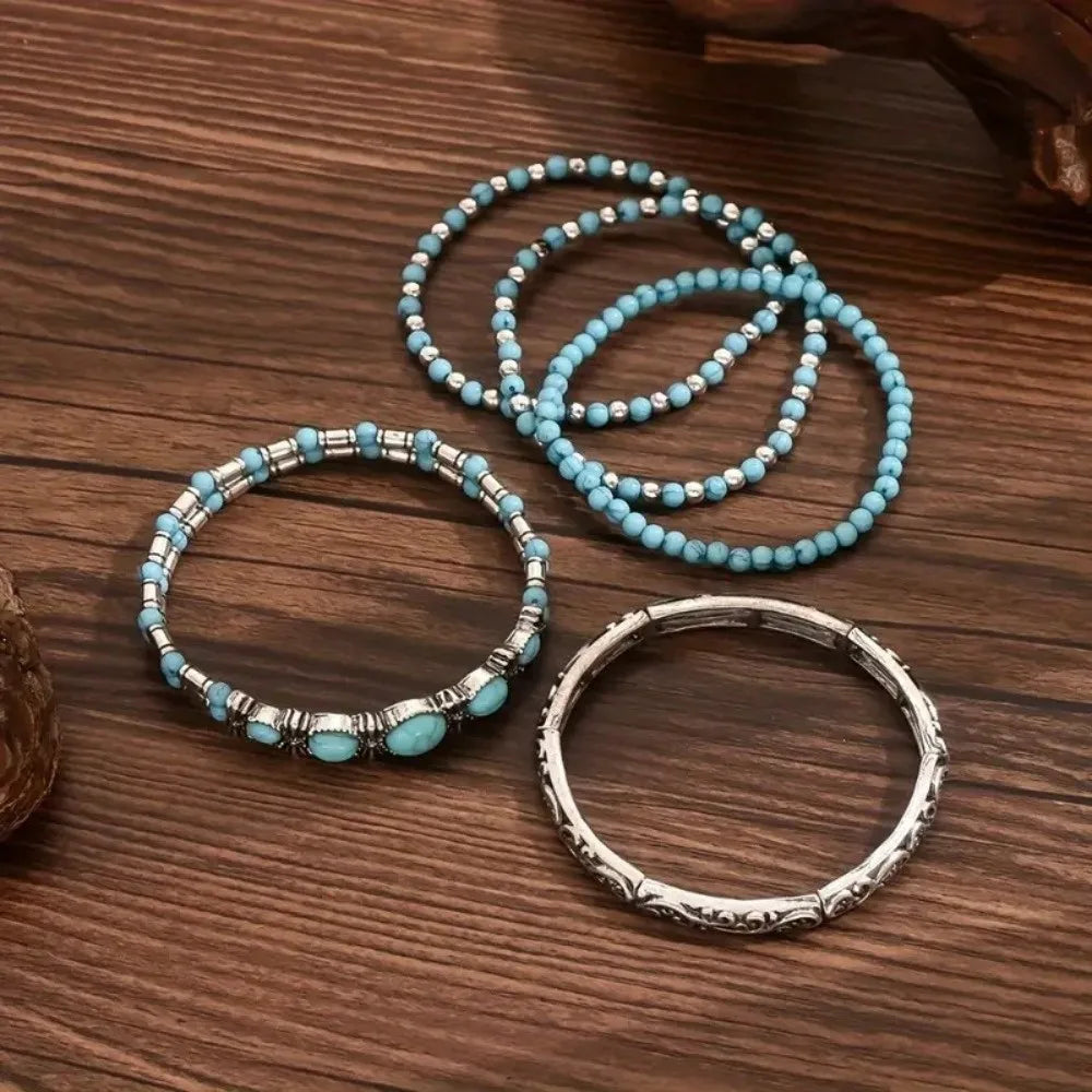 Un set de cinq bracelets perlés aux perles turquoise et argent, disposés sur une surface en bois.