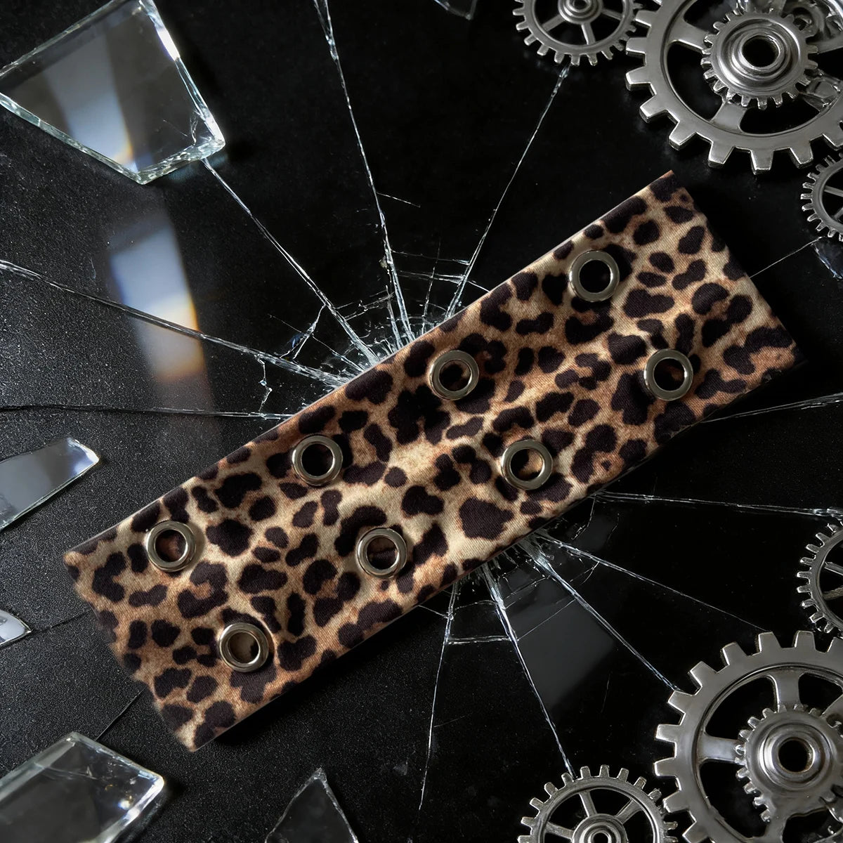 Un bandeau en œillet de punk grunge en cuir repose sur une surface de verre noir entourée d'engrenages et d'éclats métallique