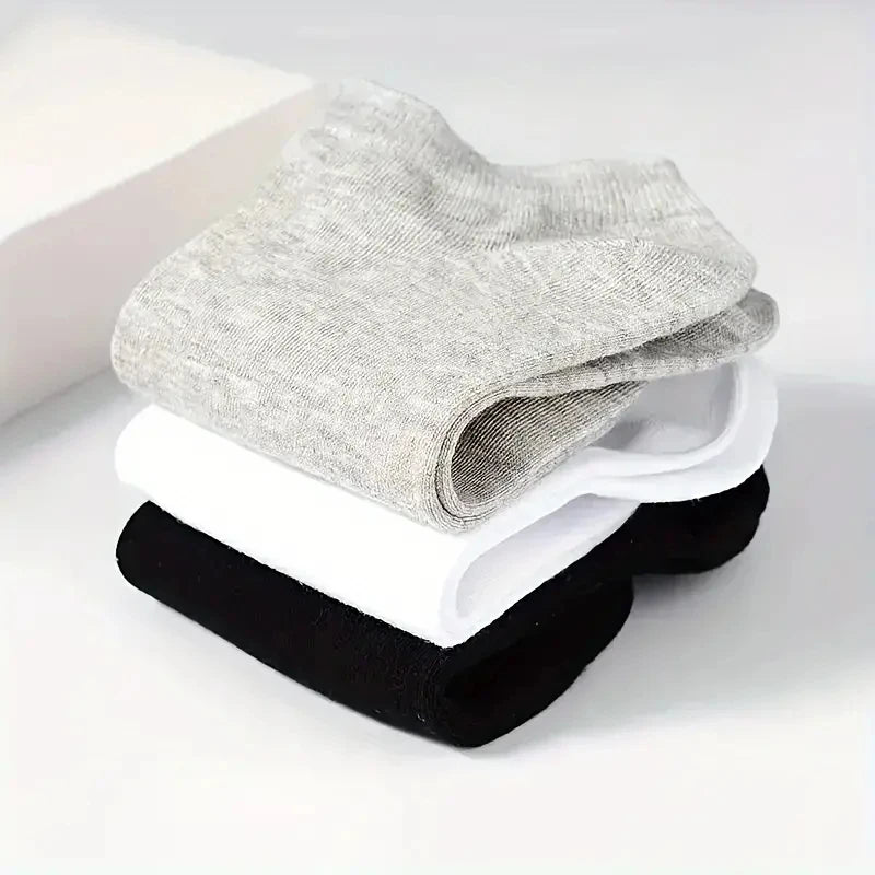 A stack of gray, white, and black comfort fit ankle socks is displayed on a white surface.