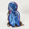 A vibrant blue satin square scarf tied around a person's hair, featuring purple and pink accents.