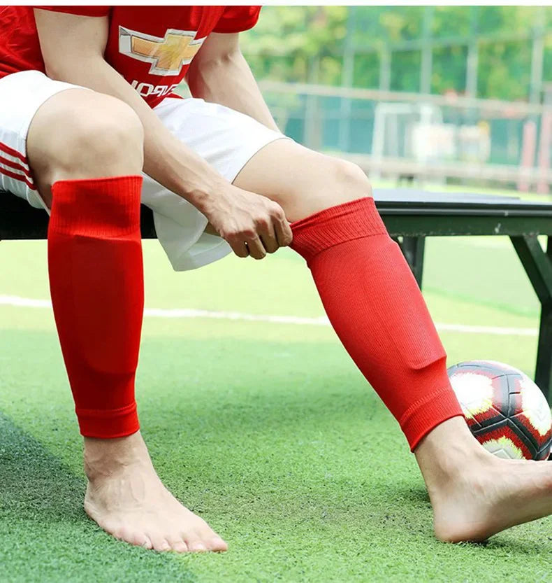 Person in red breathable football calf socks sitting on a green field.