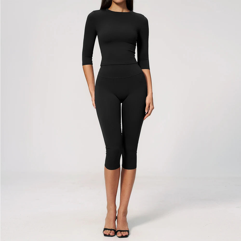 A woman wearing a black long-sleeved top and matching black leggings set for yoga and fitness.